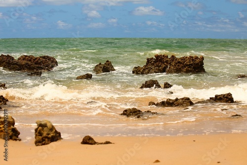Green water sea, waves breaking at water edge, dark reef rocks. Tropical beach of Tabatinga near Joao Pessoa, Paraiba state, Brazil northeast. Touristic place for vacation travel.
