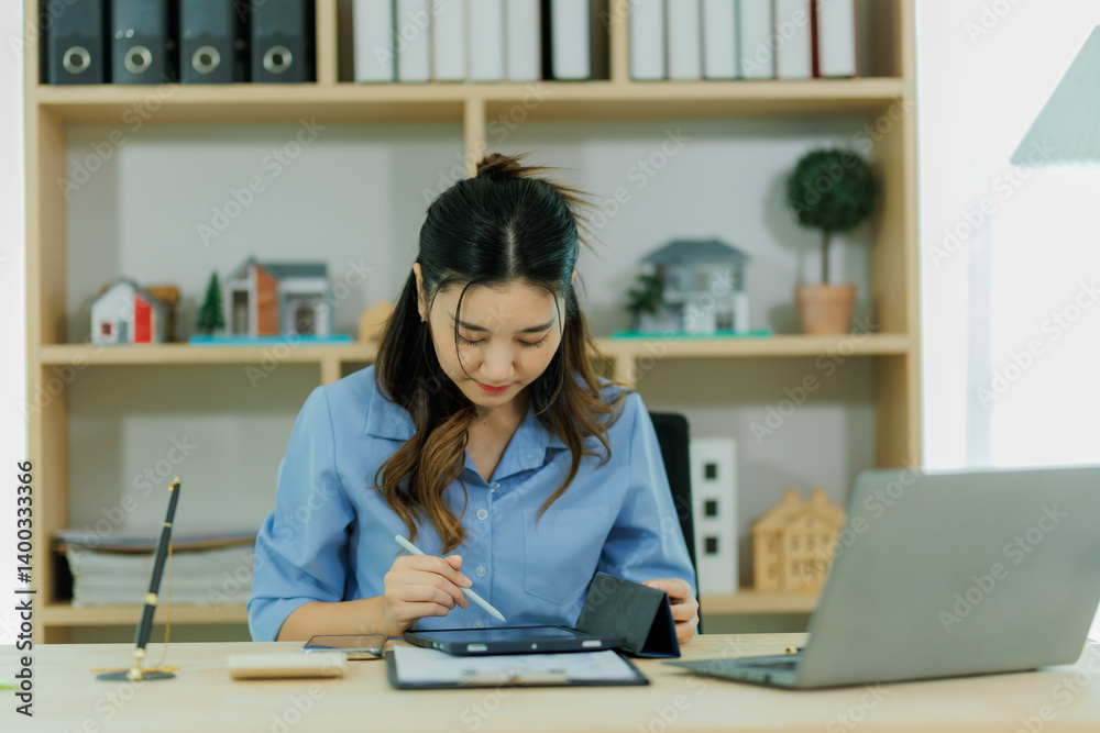 An Asian female staff member is fully engaged in preparing the monthly sales report with great focus and determination. An Asian female staff member is fully engaged in preparing the monthly sales report with great focus and determination.