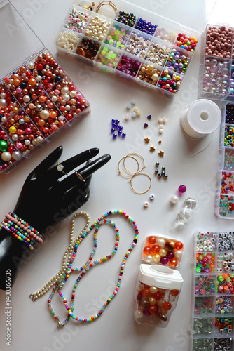 Hand figurine, colorful friendship bracelets, necklaces, various beads and DIY supplies on the table. Making jewelry at home. Flat lay.