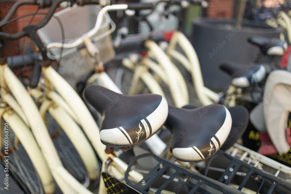 close-up view of bicycle handlebars at a bike-sharing station. The image highlights the details of the bicycle's design, showing the handlebars, grips, and lights. The background features a modern