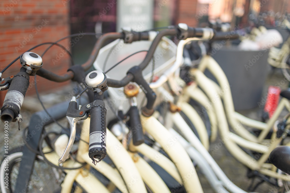 close-up view of bicycle handlebars at a bike-sharing station. The image highlights the details of the bicycle's design, showing the handlebars, grips, and lights. The background features a modern
