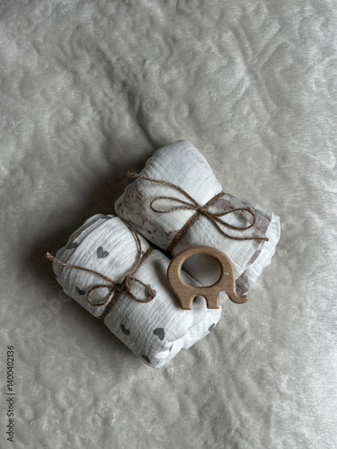 Two twisted muslin diapers and an elephant teether are lying on a milky-colored blanket. Children's fashion accessories