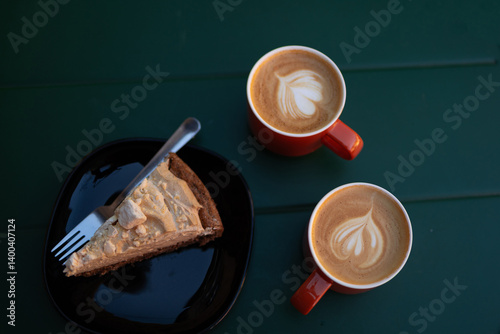 Two ceramic cups filled with rich latte coffee and a delicious piece of cake on a table in a cozy cafe. A perfect setting for enjoying a relaxing break or casual meeting with friends