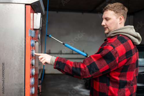 Man on manual carwash uses water isolated bill acceptor and holds a button to start a water supply. High quality photo