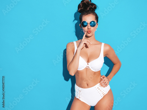 Young beautiful sexy woman with ghoul hairstyle. Trendy female in casual summer white swimsuit in sunglasses.Hot model isolated on blue. Makes duck face