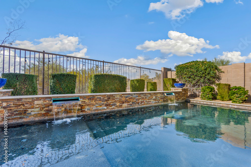 A swimming pool enclosed by a stone wall and metal fence