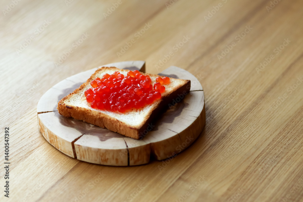 A delicious open-faced sandwich made with a slice of crusty French baguette, topped with vibrant red trout or salmon roe. Set on a rustic wooden surface