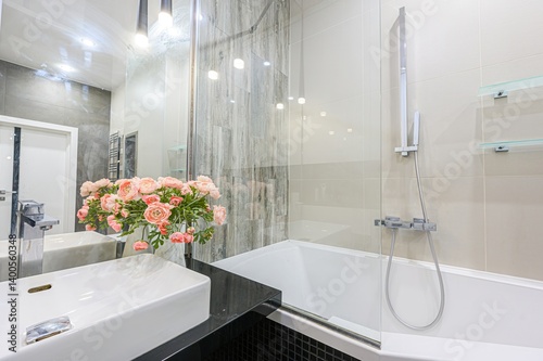 Modern bathroom featuring a white sink, bathtub, glass shower screen, and stylish gray & black accents. Flowers add a touch of elegance