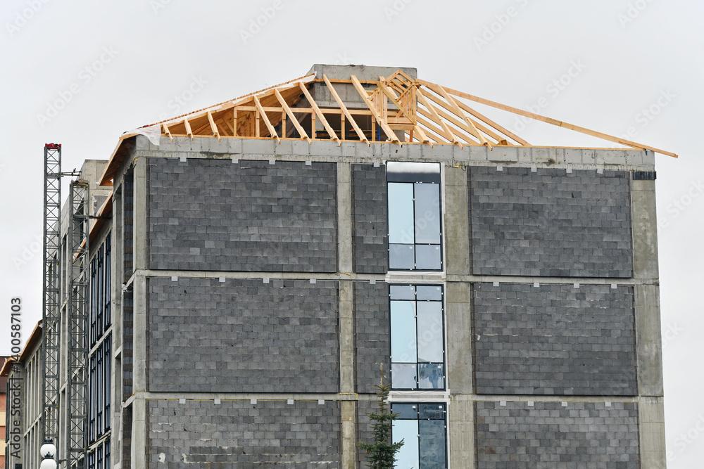 Building under construction, installing roof on modern building, installation of roof rafters, windows installation and facade insulation works. Construction site featuring building under construction