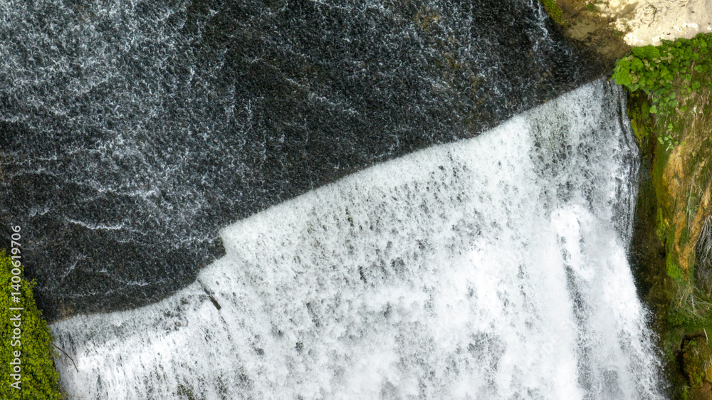Aerial closeup of a small waterfall flowing into a pond.