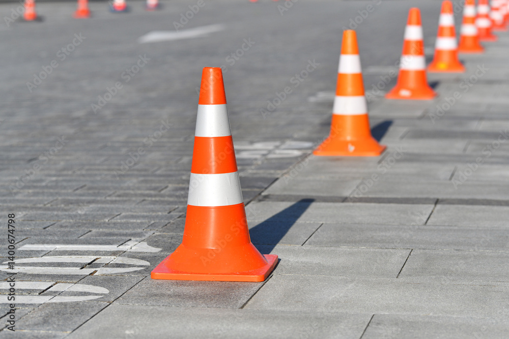 Close-up view of safety cones placed in straight line on city parking area, symbolizing restricted access. Pavement with line of reflective orange cones indicating restricted area on parking area