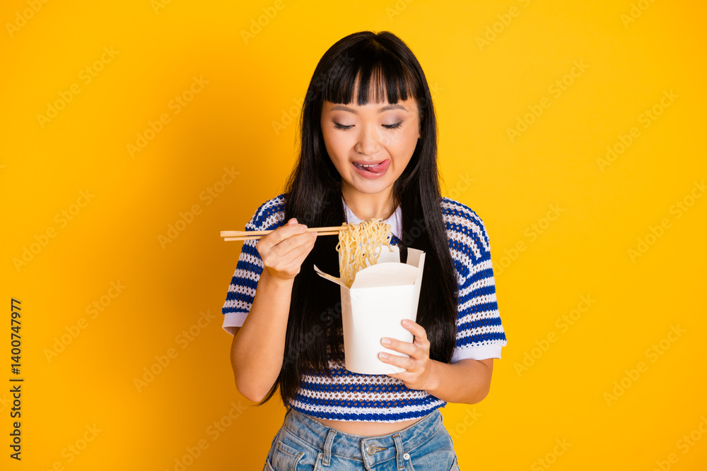 Young woman in casual style enjoying noodles with chopsticks against vibrant yellow background Young woman in casual style enjoying noodles with chopsticks against vibrant yellow background