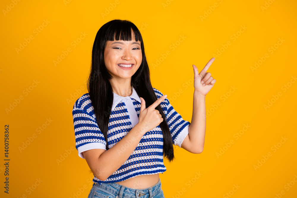Charming young woman smiling and pointing with both hands at a yellow background, wearing a stylish striped shirt and trendy casual outfit Charming young woman smiling and pointing with both hands at a yellow background, wearing a stylish striped shirt and trendy casual outfit