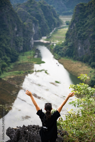 Stunning view of a girl with open arms enjoying the view from the Hang Múa Viewpoint with the a stunning landscape and the Tam Coc river in the distance. Ninh Binh, Vietnam.