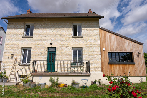 Extension moderne d’une maison en pierre beige clair avec un esprit campagnard et l'extension avec bardage en bois, contrastant harmonieusement avec la structure ancienne en pierre.