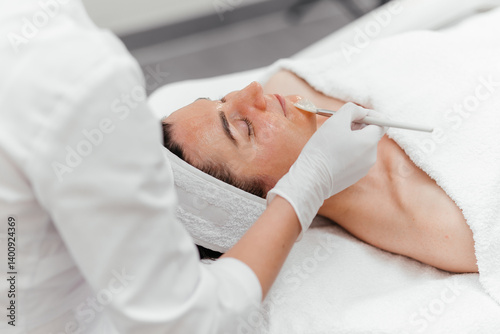 Cosmetologist cleaning face of a middle aged European woman with special gel before applying mask, peeling. Facial skin care procedures in beauty salon. Rejuvenation wellness, white background