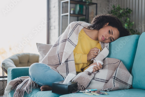 Young sad woman resting at home on a cozy couch wrapped in a blanket, feeling unwell