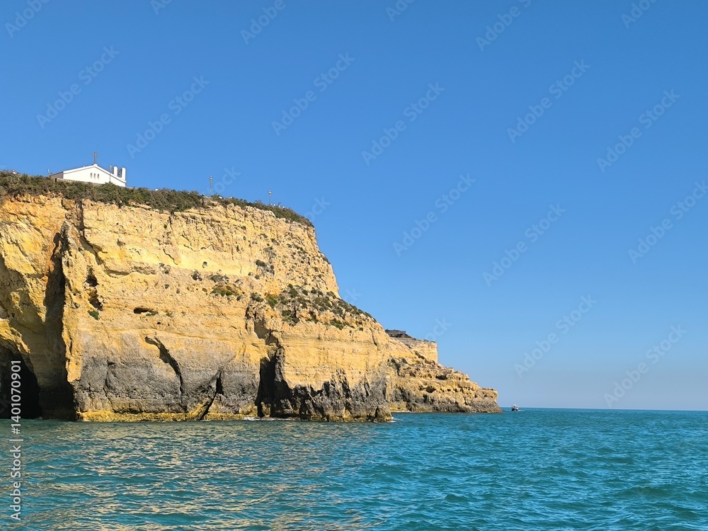 Fototapeta premium The rugged cliffside rises above the turquoise sea, creating a dramatic coastal scene with clear waters below.