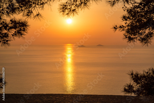 Sunset over the sea with a view of islands and coastal cliffs, framed by trees