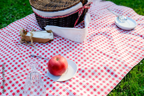 Picnic basket and apple on a red checkered tablecloth outside on fresh air
