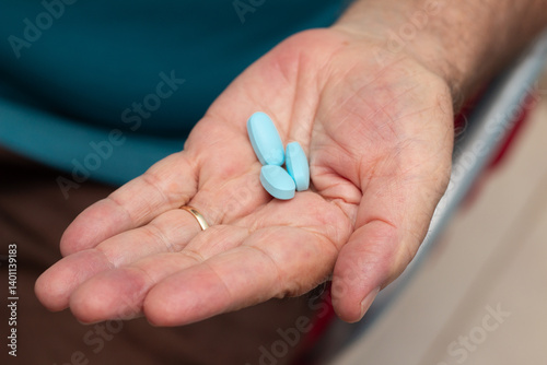 Mão de um homem idoso com três comprimidos azuis de viagra.