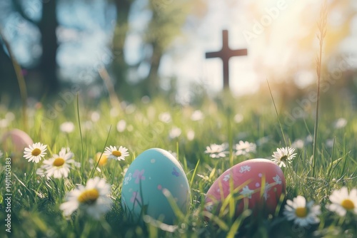Colorful Easter eggs in the grass with daisies and copy space for text, blurred background of an Easter landscape with a white church cross, bright sunny day, sunlight, happy holiday concept