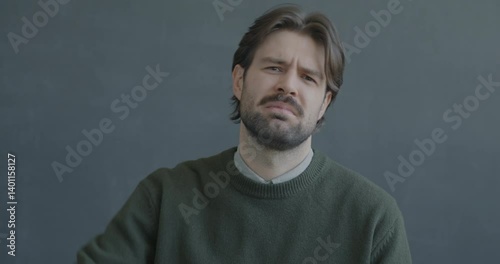 Portrait of displeased young man showing thumbs-down hand gesture looking at camera expressing disappointment on black color background.