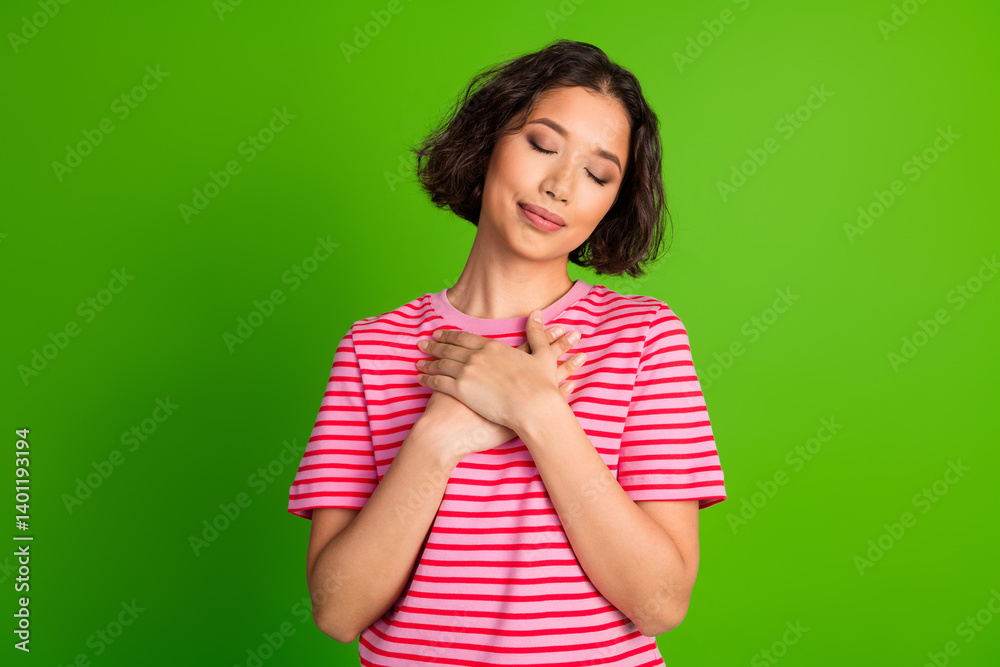 Young woman with a serene expression holding hands to her chest against a vibrant green background Young woman with a serene expression holding hands to her chest against a vibrant green background