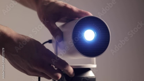 Close up, man's hand adjusting angle of lens modern wi-fi video-projector with lighting blue light. Video or photo presentation and home movie watching. 4k footage.