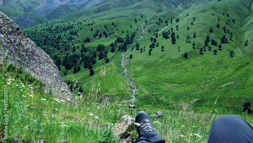 legs of a resting tourist with a view of large green hills, Kyrtyk gorge, Elbrus National Park, Caucasus, Kabardino-Balkaria in summer