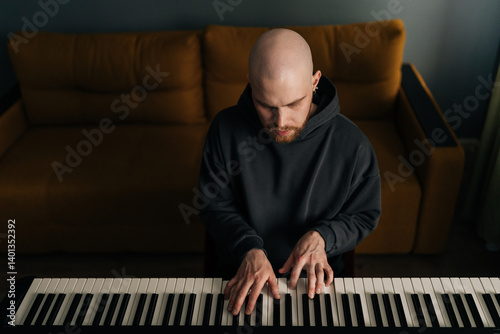 Foto Young bald bearded man composer playing synthesizer in living room sitting on chair