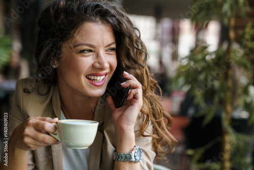 Smiling Caucasian Woman Talking on Phone While Enjoying Coffee in Bright Eco-Friendly Coffee Shop