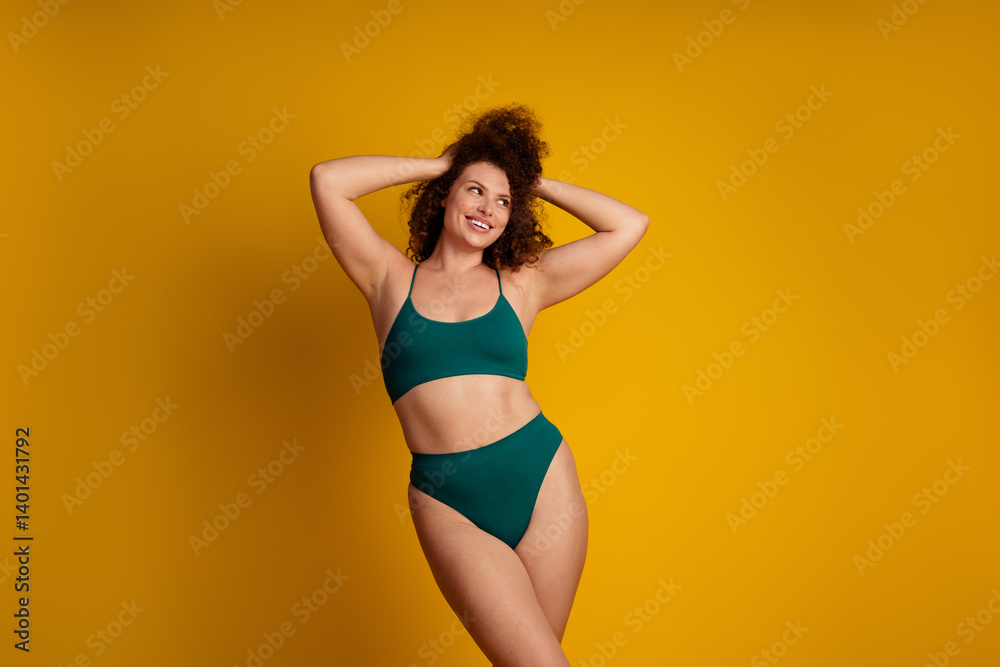 Obraz premium Confident young woman in green lingerie posing naturally against a bright yellow background, promoting self acceptance, body positivity