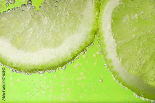 Soda water with lime slices against light green background, closeup