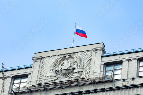 Russian flag - white, blue and red colors on the building of The State Duma of the Russian Federation - the Russian Parliament with blue sky background