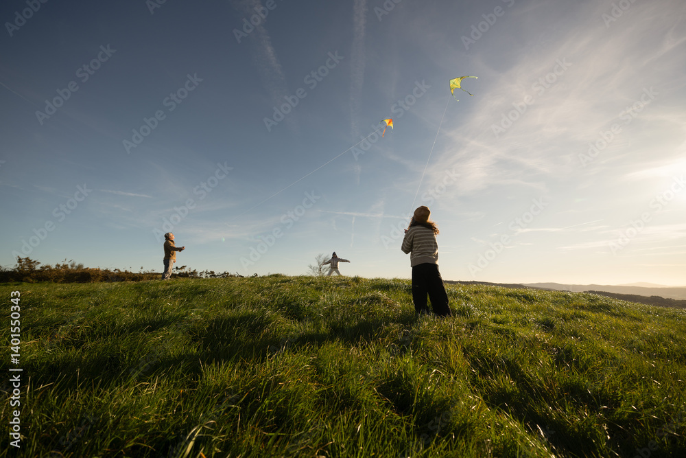Fototapeta premium Father and daughters flying kites in a green meadow on windy day
