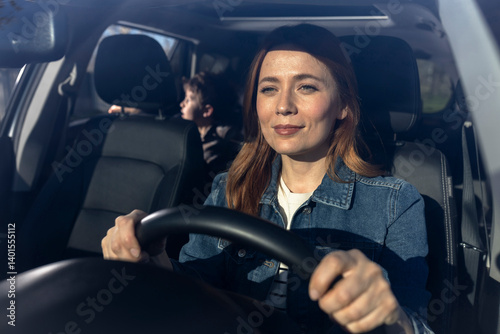 Happy young woman driving a car with a kid in the backseat