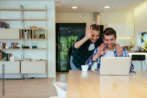 Obraz na płótnie A young married couple is talking to parents, family and friends on a video call via a laptop while sitting in the living room of their modern house. w salonie