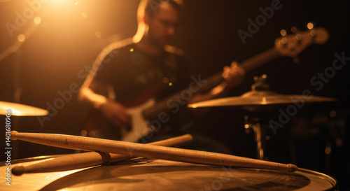 Drumsticks resting on snare drum with bassist in background atmospheric stage lighting live music performance concept