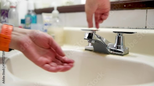 Two hands are going to wash their hands using the metal faucet in the bathroom sink, water service suspended, a topic of savings and hygiene