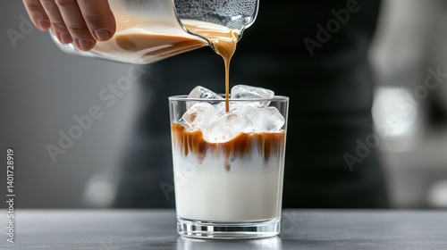 A barista pouring fresh espresso over ice and milk in a clear glass, showing the beautiful layers of the iced coffee drink.