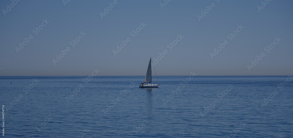 Obraz premium Sailboat sailing in a calm blue sea under a clear sky