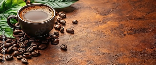 A dark cup of coffee with beans scattered around, leaves on a brown surface