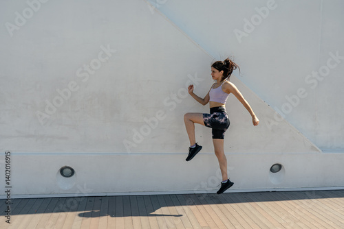 Obraz na płótnie Young sporty woman doing high knee exercise outdoors against white wall w salonie