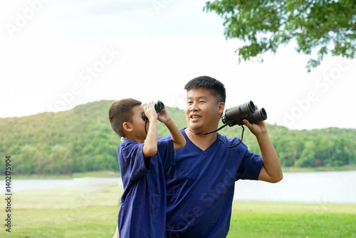 A father teaches his son how to use binoculars to look at nature, birds, and wildlife in national parks while taking the family on a camping holiday.