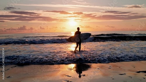 Silhouette of a surfer walking along the beach at sunset, captured from a low angle. The video conveys a serene, adventurous vibe.