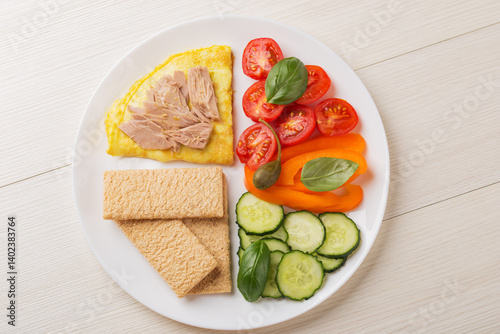 Harvard plate with omelette, tuna, vegetables, whole grain chips on white wooden table. Balanced Harvard breakfast plate.