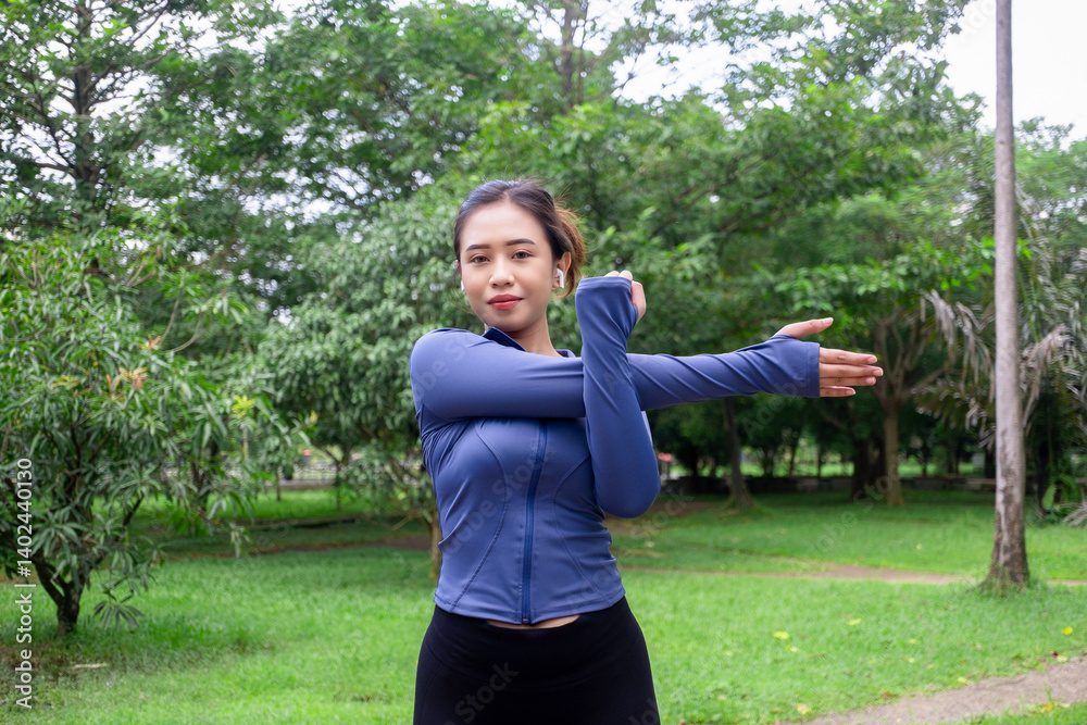 Confident woman doing arm stretch outdoors in a lush green park Confident woman doing arm stretch outdoors in a lush green park
