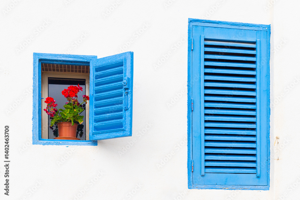 Two blue windows with shutters on a white wall of a house.