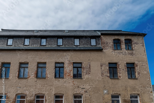 Old stone building with multiple windows under a cloudy sky in a quaint town setting
